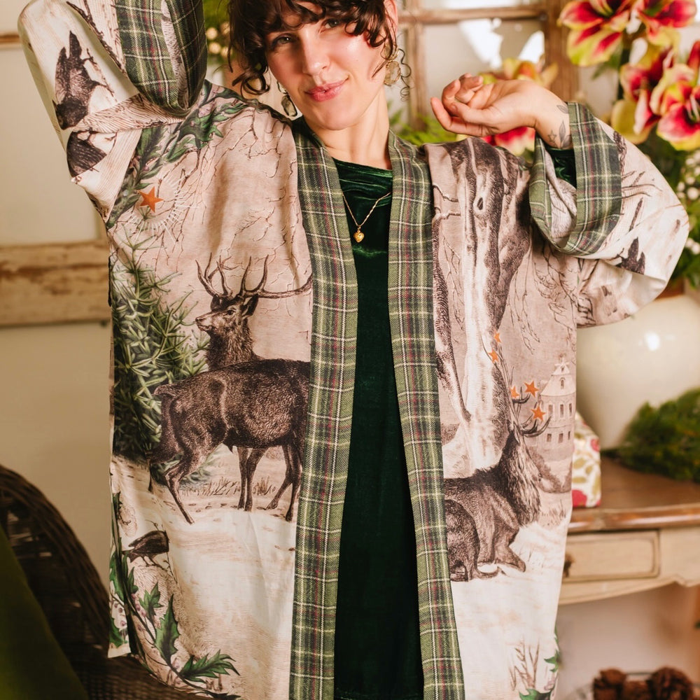 
                  
                    Model wearing a bamboo viscose mid-length duster with Victorian-era images from holiday greeting cards — including reindeer in the snow, a little fir tree, golden stars, and traditional plaid trim - Market of Stars
                  
                