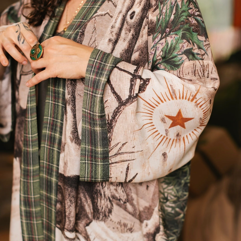
                  
                    Model wearing a bamboo viscose mid-length duster with Victorian-era images from holiday greeting cards — including reindeer in the snow, a little fir tree, golden stars, and traditional plaid trim - Market of Stars
                  
                