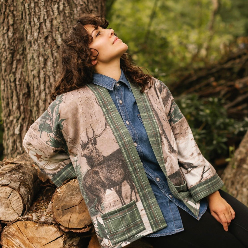 Model wearing a fleece lined jacket with pockets with Victorian-era images from holiday greeting cards — including reindeer in the snow, a little fir tree, golden stars, and traditional plaid trim - Market of Stars