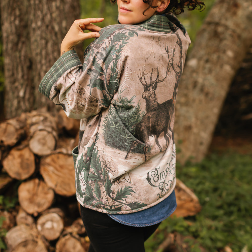 
                  
                    Model wearing a fleece lined jacket with pockets with Victorian-era images from holiday greeting cards — including reindeer in the snow, a little fir tree, golden stars, and traditional plaid trim - Market of Stars
                  
                