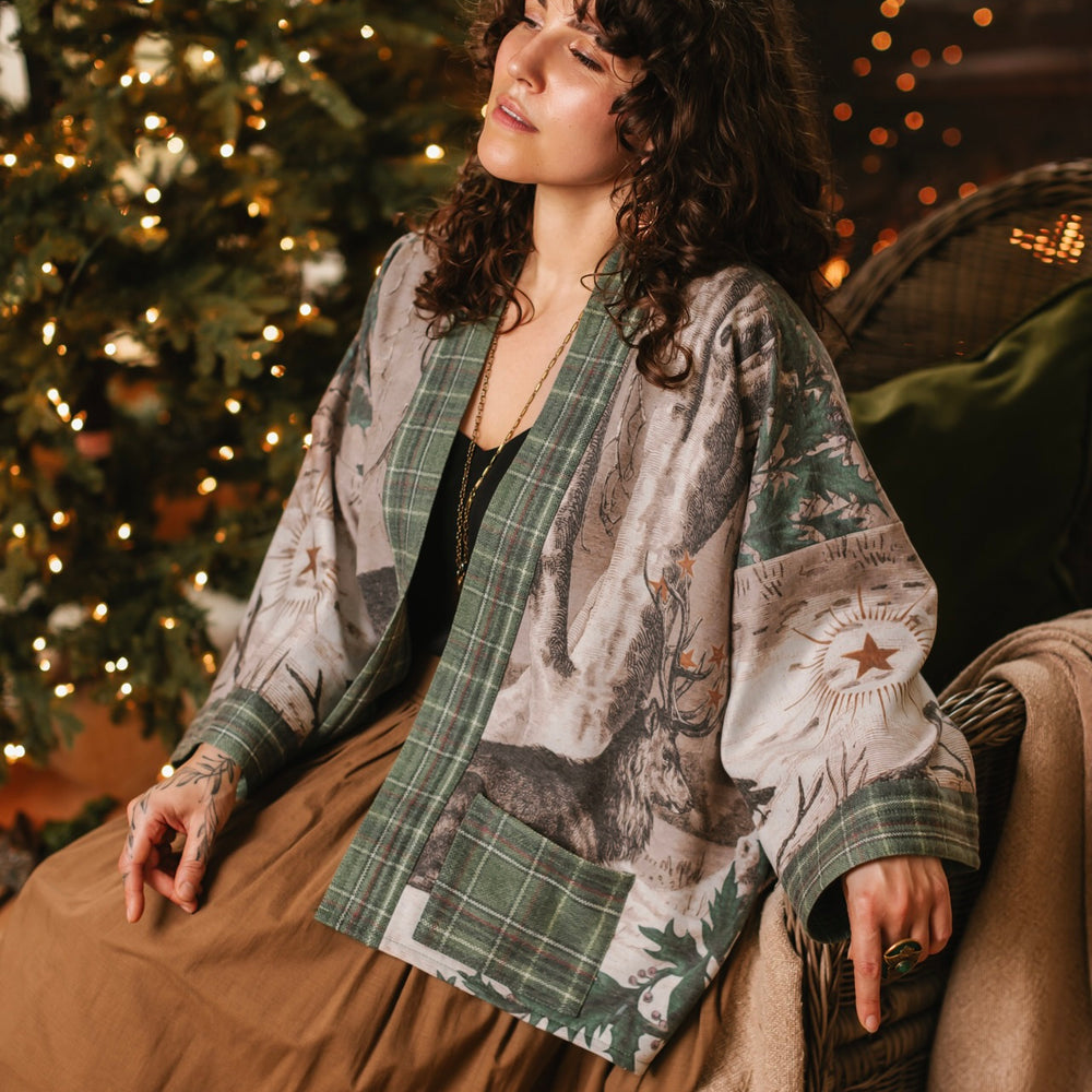 
                  
                    Model wearing a fleece lined jacket with pockets with Victorian-era images from holiday greeting cards — including reindeer in the snow, a little fir tree, golden stars, and traditional plaid trim - Market of Stars
                  
                