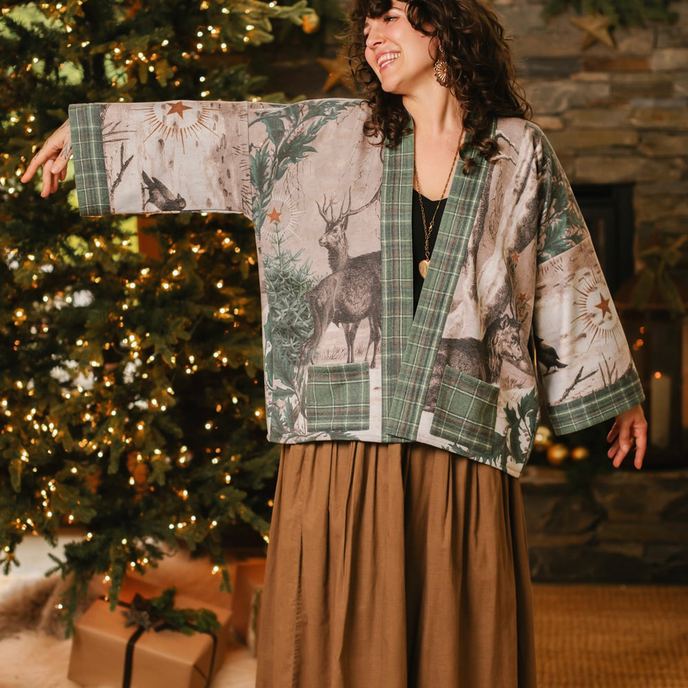 
                  
                    Model wearing a fleece lined jacket with pockets with Victorian-era images from holiday greeting cards — including reindeer in the snow, a little fir tree, golden stars, and traditional plaid trim - Market of Stars
                  
                