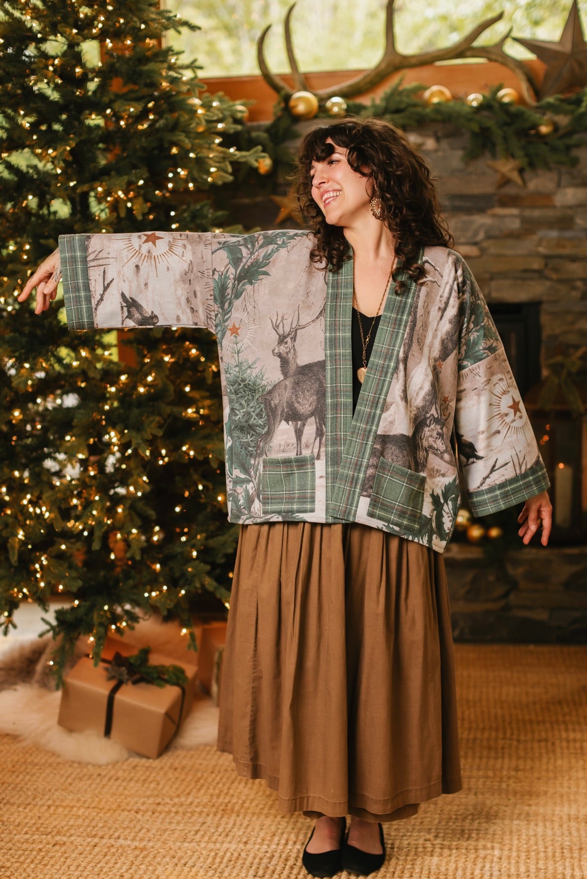 Model wearing a fleece lined jacket with pockets with Victorian-era images from holiday greeting cards — including reindeer in the snow, a little fir tree, golden stars, and traditional plaid trim - Market of Stars