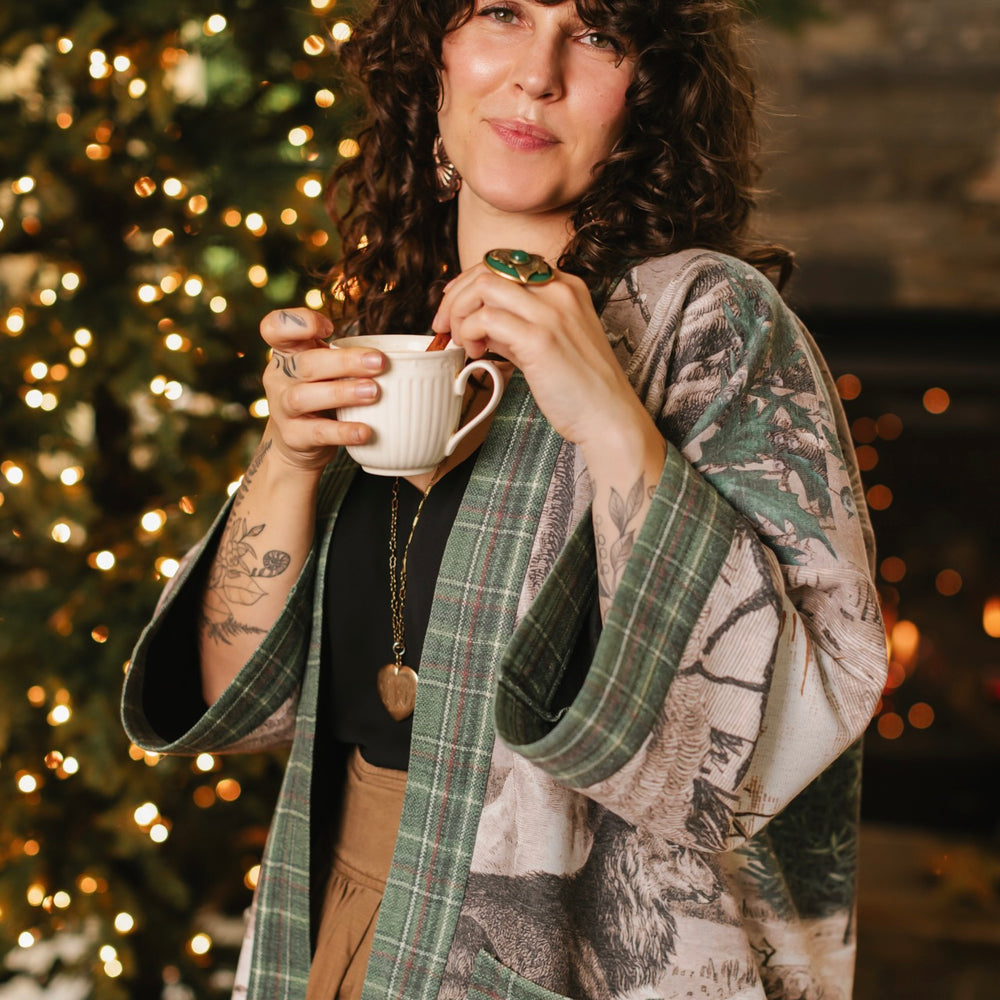 
                  
                    Model wearing a fleece lined jacket with pockets with Victorian-era images from holiday greeting cards — including reindeer in the snow, a little fir tree, golden stars, and traditional plaid trim - Market of Stars
                  
                