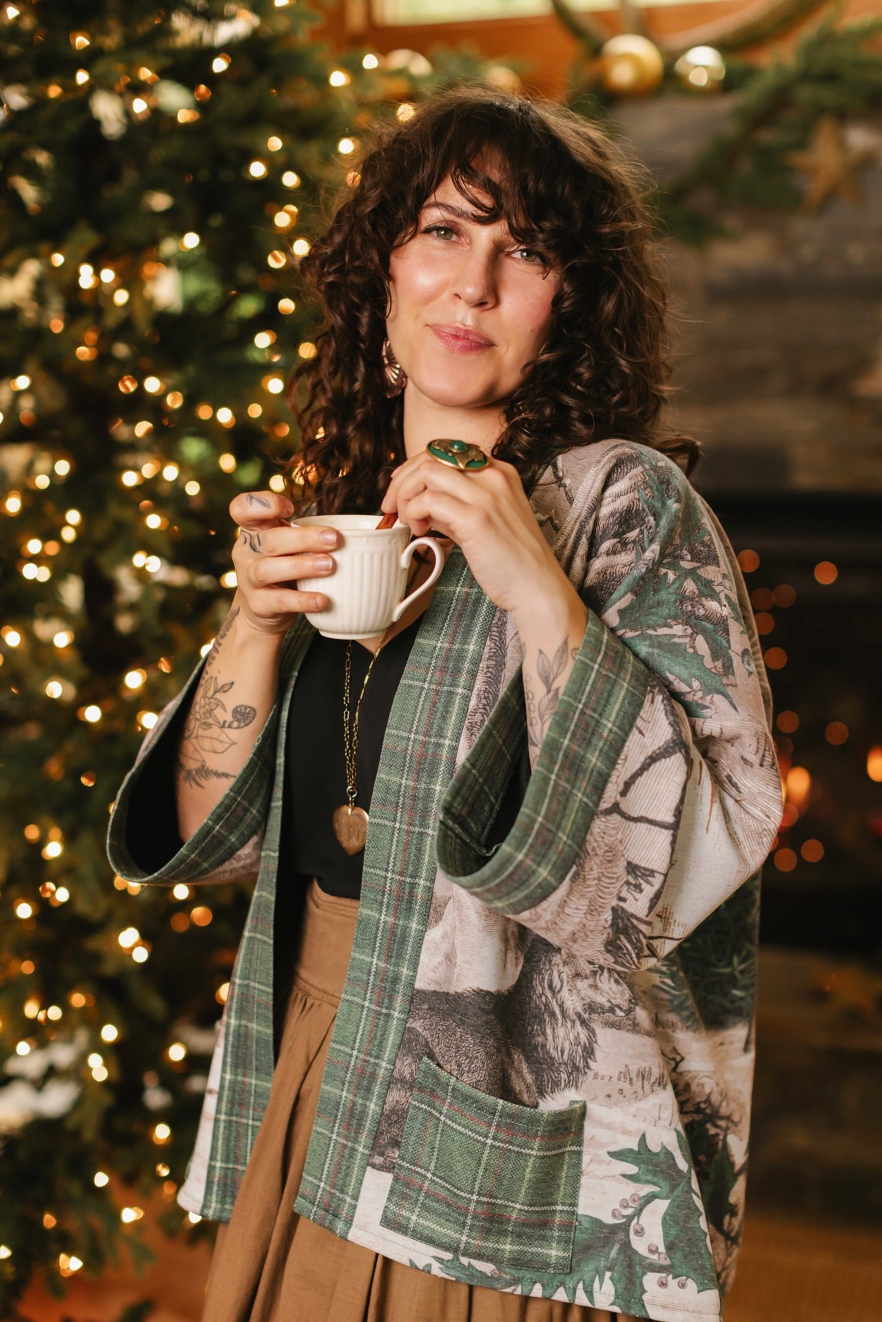 Model wearing a fleece lined jacket with pockets with Victorian-era images from holiday greeting cards — including reindeer in the snow, a little fir tree, golden stars, and traditional plaid trim - Market of Stars
