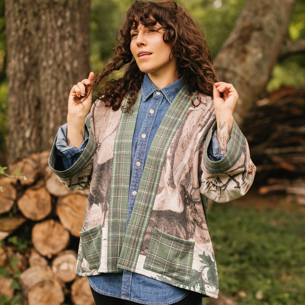 
                  
                    Model wearing a fleece lined jacket with pockets with Victorian-era images from holiday greeting cards — including reindeer in the snow, a little fir tree, golden stars, and traditional plaid trim - Market of Stars
                  
                
