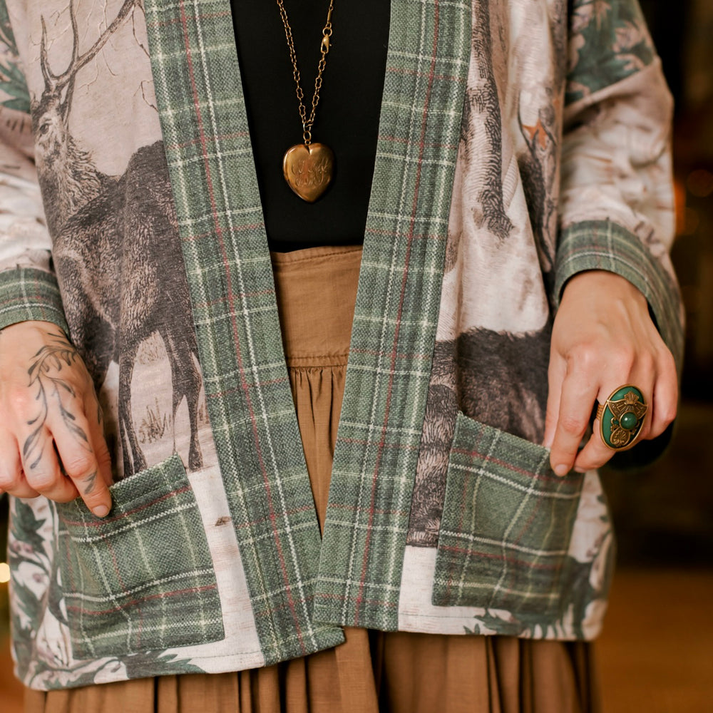 
                  
                    Model wearing a fleece lined jacket with pockets with Victorian-era images from holiday greeting cards — including reindeer in the snow, a little fir tree, golden stars, and traditional plaid trim - Market of Stars
                  
                
