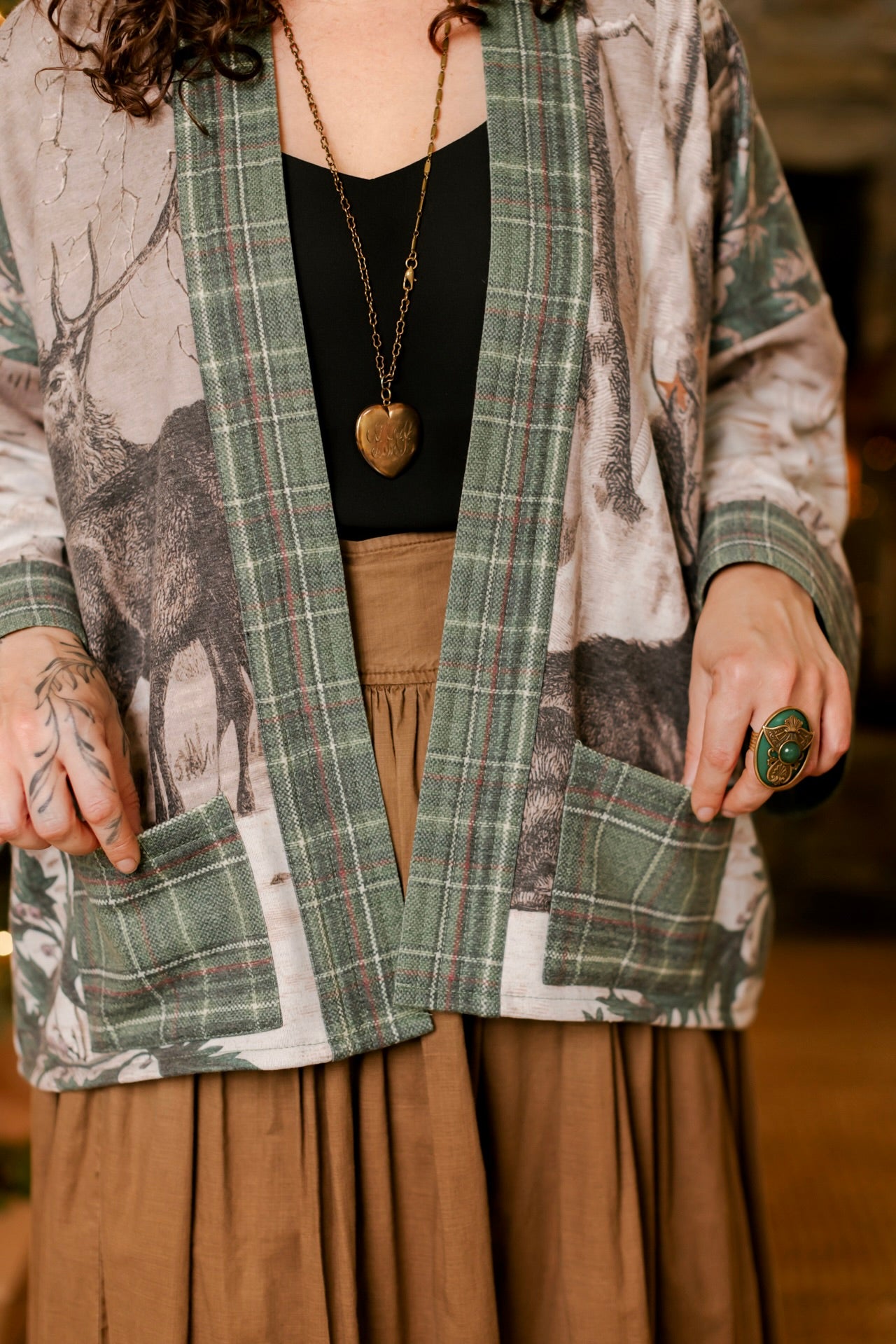 Model wearing a fleece lined jacket with pockets with Victorian-era images from holiday greeting cards — including reindeer in the snow, a little fir tree, golden stars, and traditional plaid trim - Market of Stars