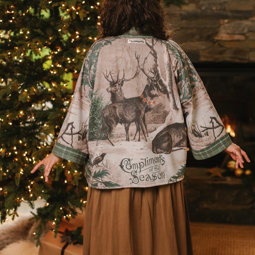 
                  
                    Model wearing a fleece lined jacket with pockets with Victorian-era images from holiday greeting cards — including reindeer in the snow, a little fir tree, golden stars, and traditional plaid trim - Market of Stars
                  
                