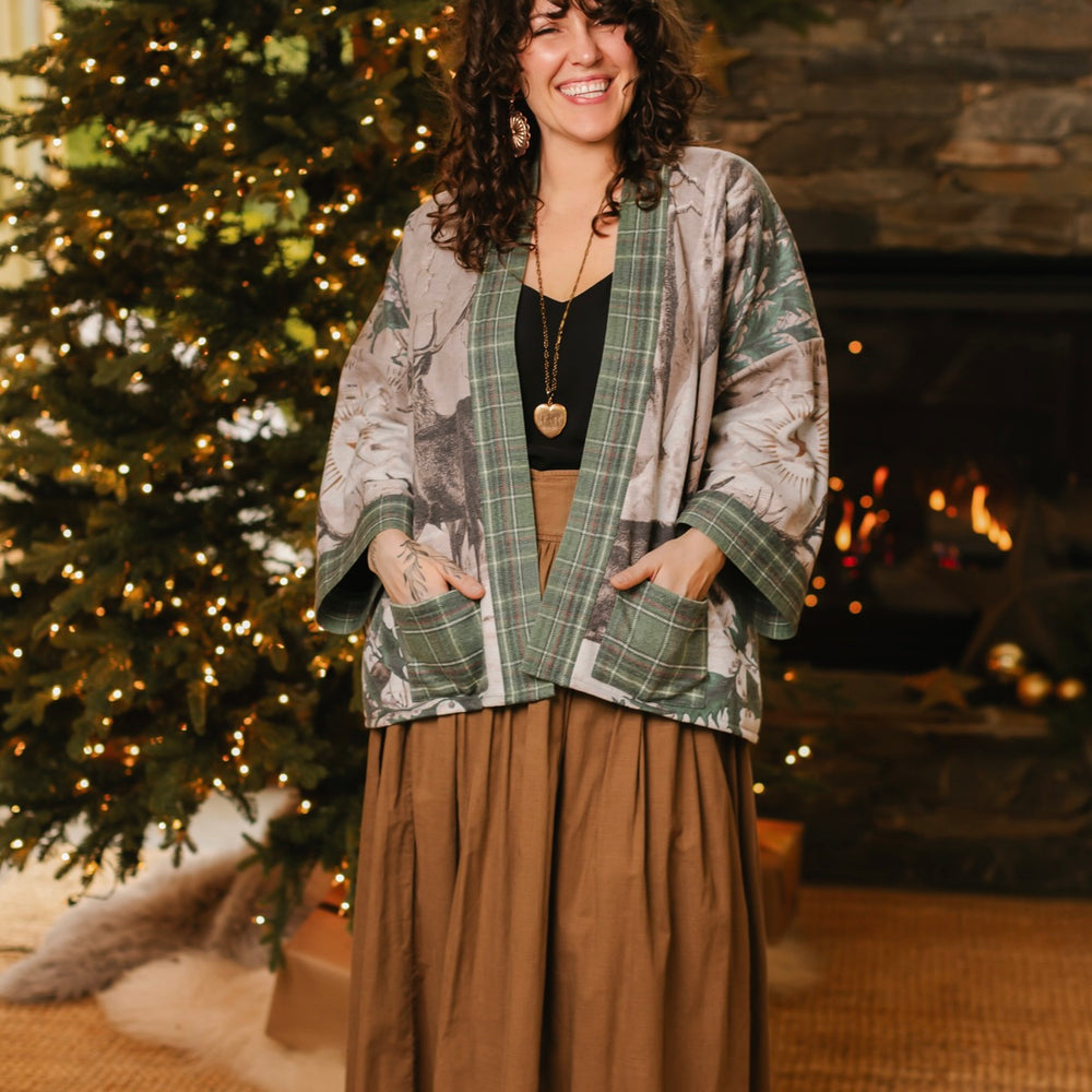 
                  
                    Model wearing a fleece lined jacket with pockets with Victorian-era images from holiday greeting cards — including reindeer in the snow, a little fir tree, golden stars, and traditional plaid trim - Market of Stars
                  
                