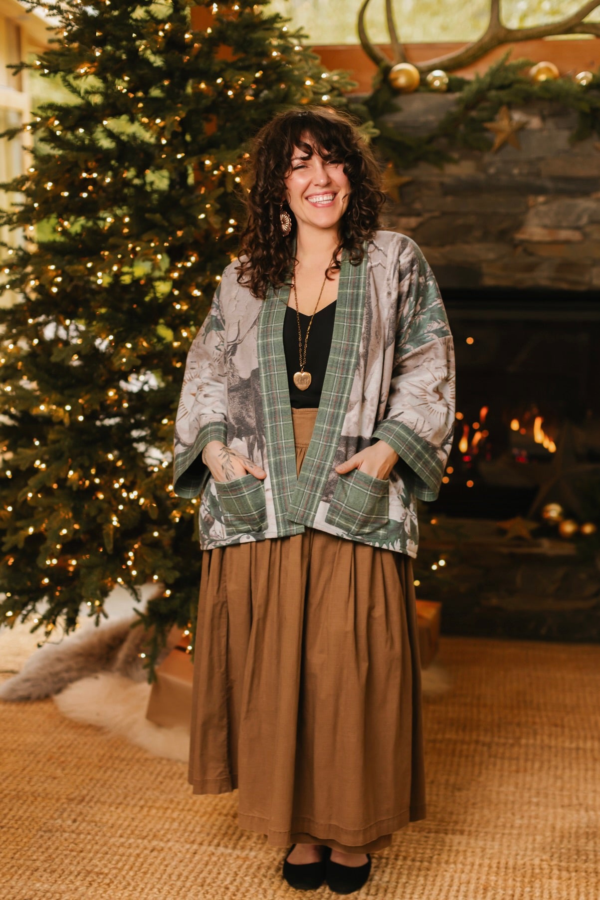 Model wearing a fleece lined jacket with pockets with Victorian-era images from holiday greeting cards — including reindeer in the snow, a little fir tree, golden stars, and traditional plaid trim - Market of Stars