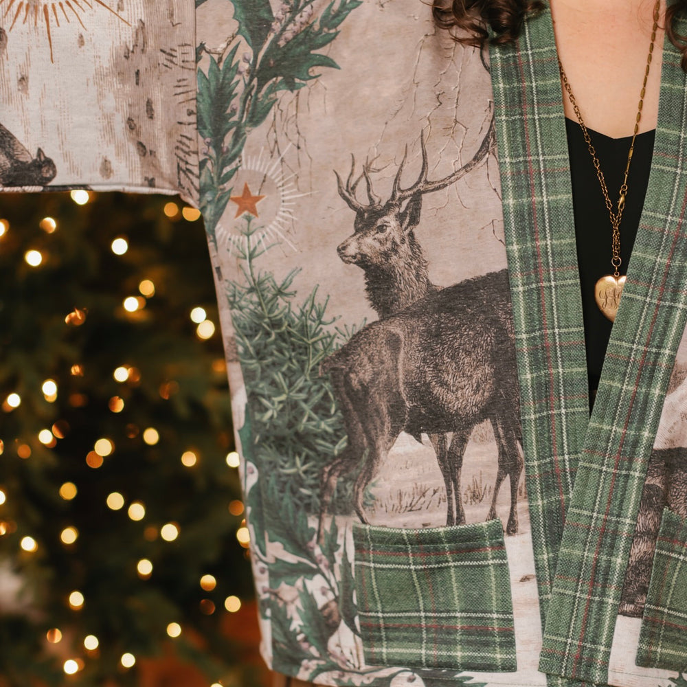 
                  
                    Model wearing a fleece lined jacket with pockets with Victorian-era images from holiday greeting cards — including reindeer in the snow, a little fir tree, golden stars, and traditional plaid trim - Market of Stars
                  
                