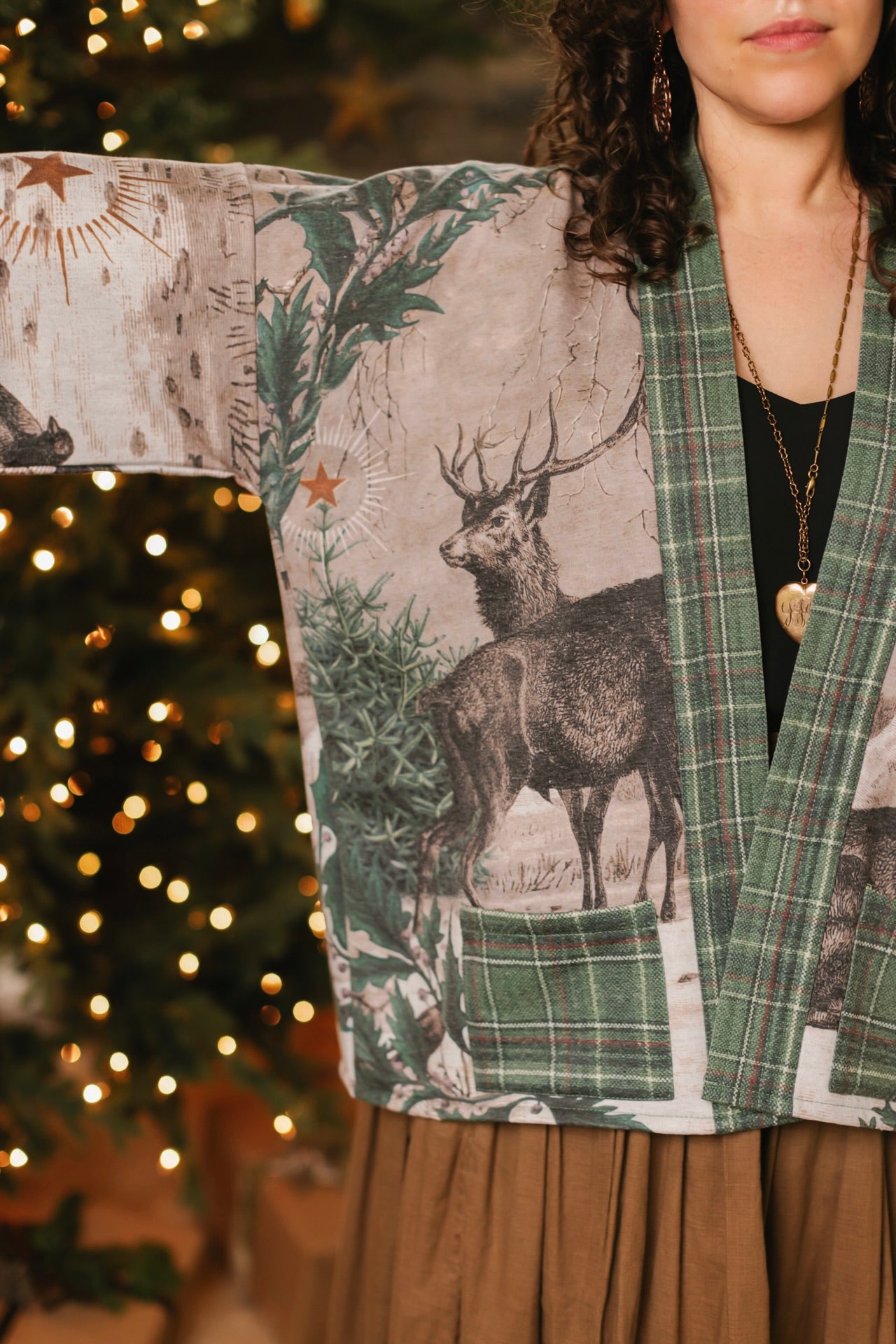 Model wearing a fleece lined jacket with pockets with Victorian-era images from holiday greeting cards — including reindeer in the snow, a little fir tree, golden stars, and traditional plaid trim - Market of Stars
