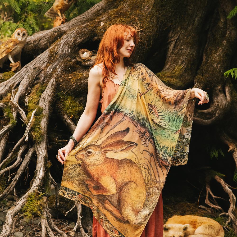 Model wearing a bamboo-viscose scarf where a noble rabbit rests deep within an underground burrow, surrounded by the warmth and safety of the earth. Created in collaboration with Charles van Sandwyck - Market of Stars